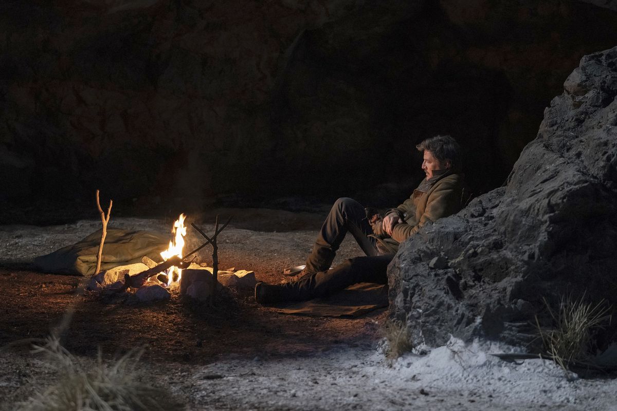 Joel (Pedro Pascal) が座って岩壁にもたれかかり、火を見ている