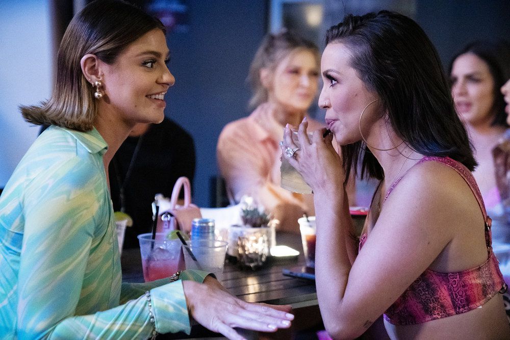 Raquel Leviss and Scheana Shay sit facing each other at a table with drinks and candles on it. Scheana leans forward appearing to eagerly listen while Raquel talks in this still from Vanderpump Rules season 10.