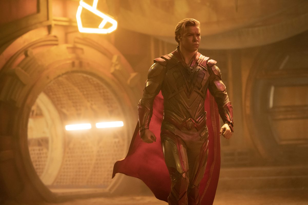 Adam Warlock (do Will Poulter thủ vai), một hình người da vàng với áo giáp vàng và đỏ và áo choàng đỏ, sải bước qua một tòa nhà trong Guardians of the Galaxy Vol. 3