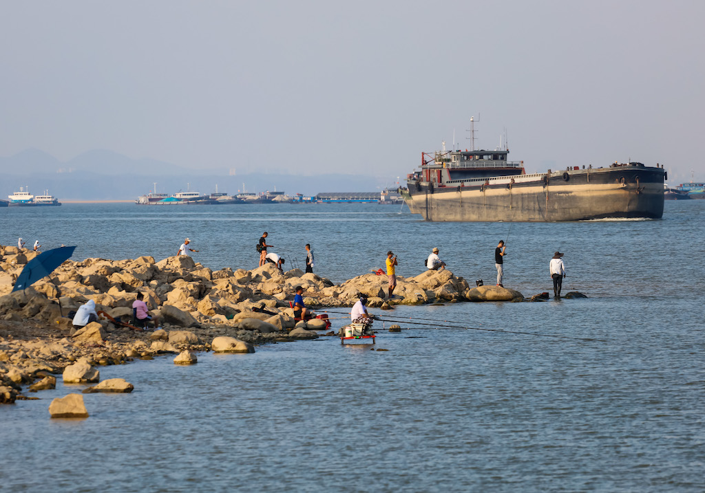 28年2022月XNUMX日、暑い日に中国最大の淡水湖、鄱陽湖沿いを航行する貨物船で釣りをする人々。XNUMX年XNUMX月XNUMX日。