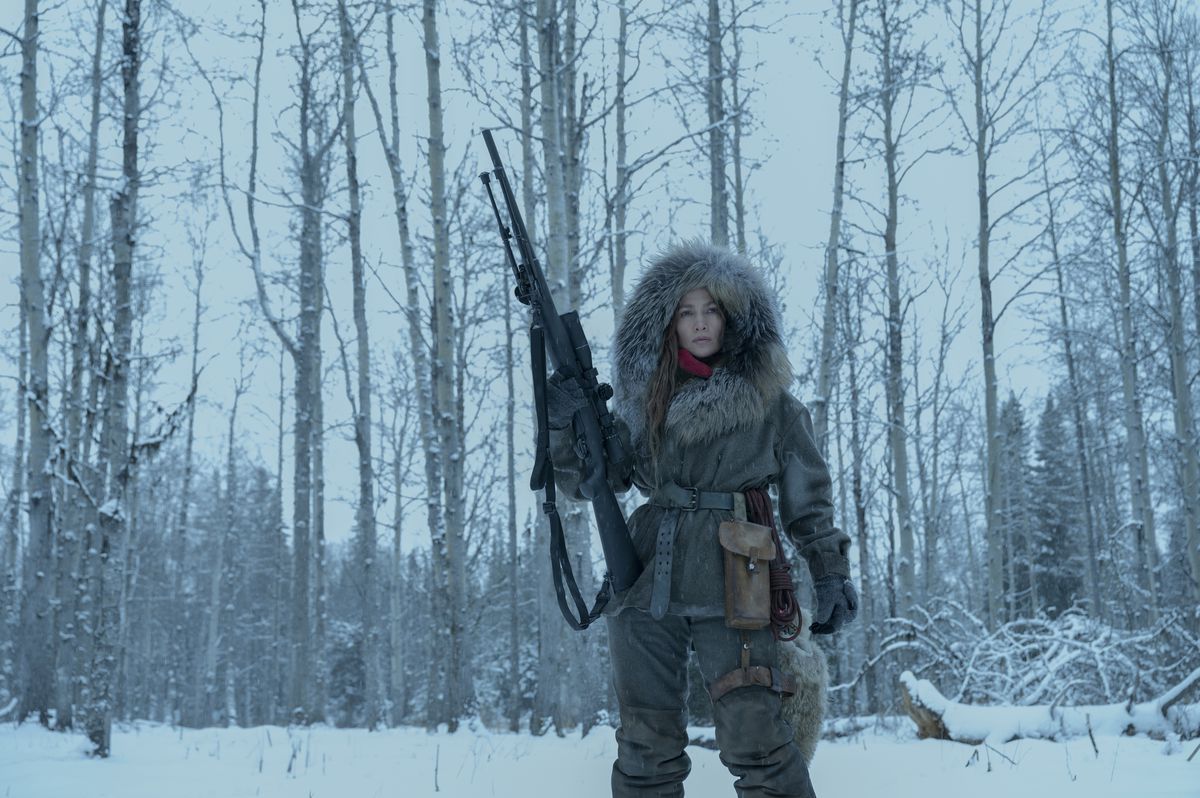 جينيفر لوبيز بدور "الأم" ، قاتل يرتدي معطفاً شتوياً يحمل بندقية في وركها ، في فيلم The Mother.