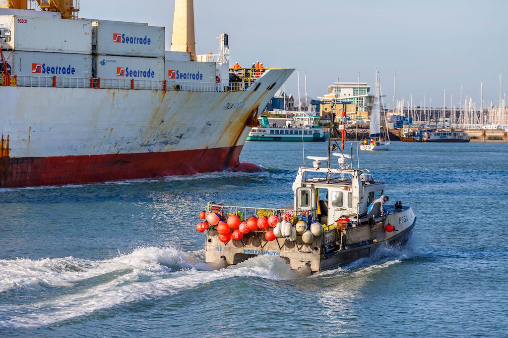 18年2020月XNUMX日、ポーツマス港のゴスポート近くで大型コンテナ船の横を通り過ぎる伝統的な小型漁船が小さく見えた。