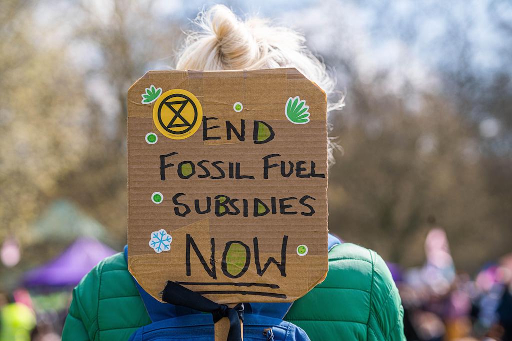 Extinction Rebellion'dan bir iklim aktivisti, 9 Nisan 2022'de iklim adaleti ve fosil yakıt ekonomisine son verilmesi talebiyle Londra'nın merkezine yürümeden önce Hyde Park'ta "Fosil yakıt sübvansiyonlarına son verin" tabelasını tutuyor.