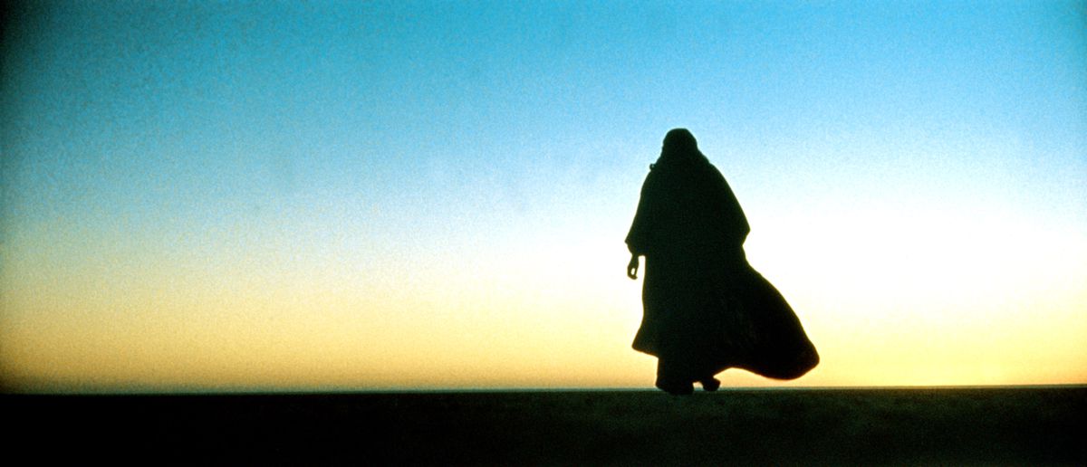 Un hombre con traje beduino tradicional se recorta contra un cielo de puesta de sol del desierto