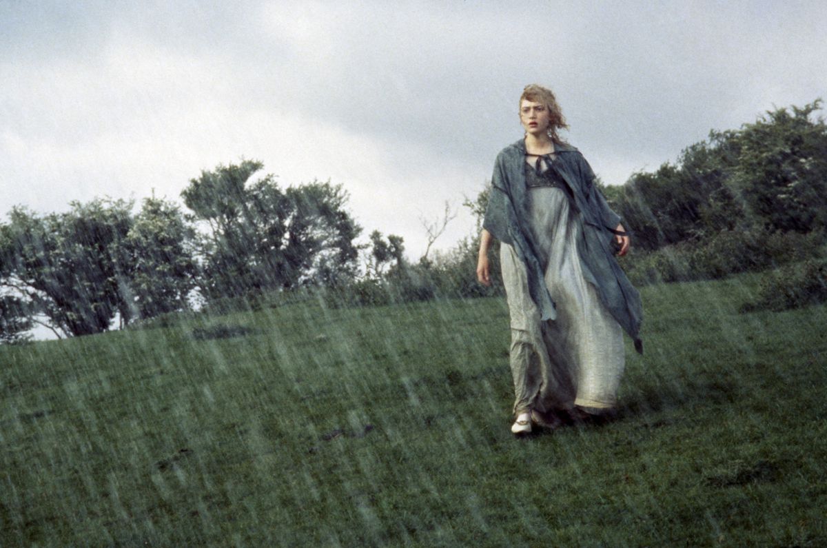 Kate Winslet camina bajo una fuerte lluvia en un páramo, vestida con atuendo Regency