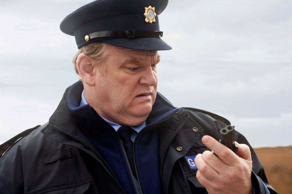 Brendan Gleeson, vestido de policía, mira consternado una pequeña pistola que tiene en la mano.