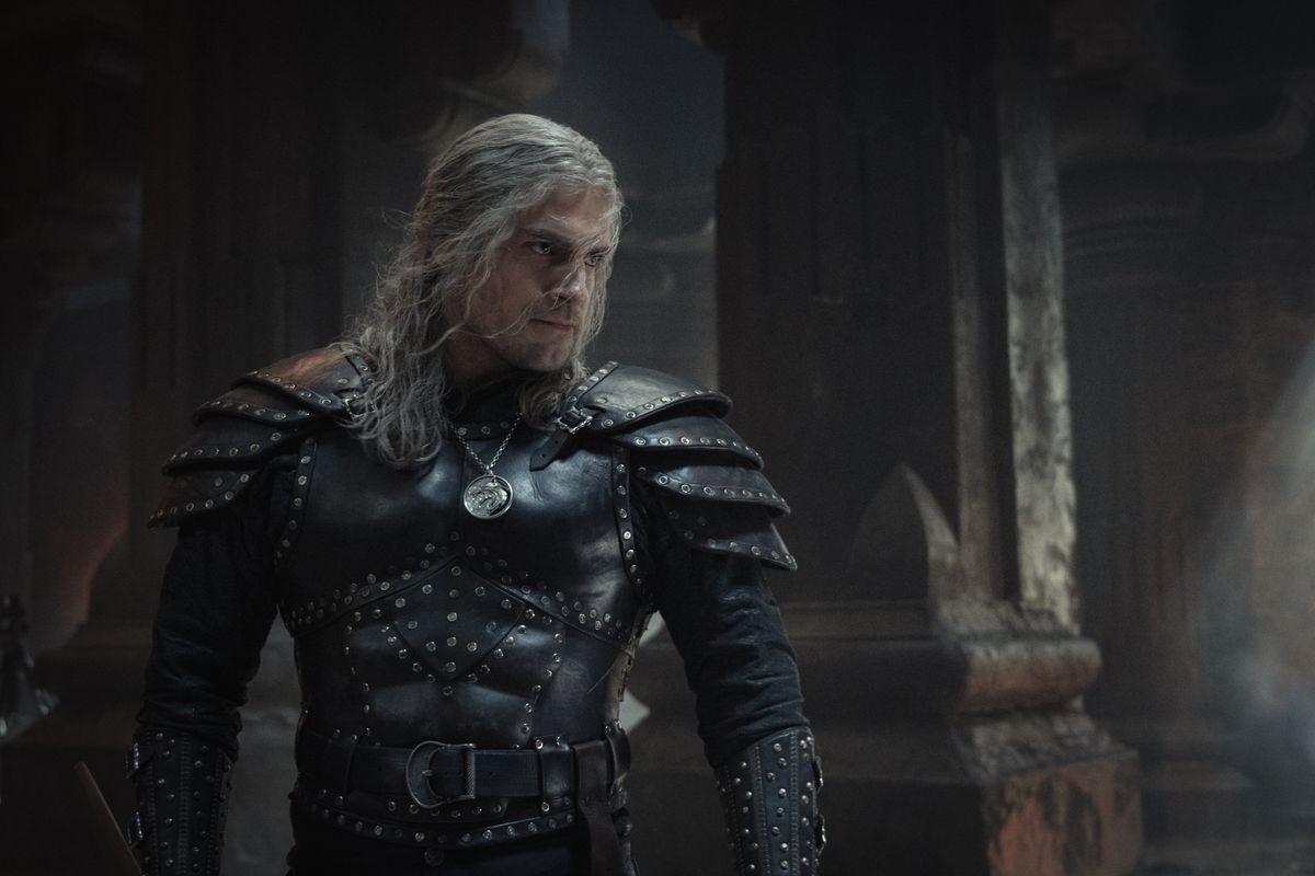 Henry Cavill pose dans une grande armure cloutée noire dans une zone de type château, prêt à frapper un gars dans The Witcher