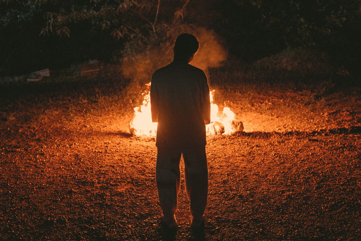 Prime Video의 Swarm 예고편에서 한 인물이 밤에 숲 한가운데 모닥불 앞에 서 있습니다.
