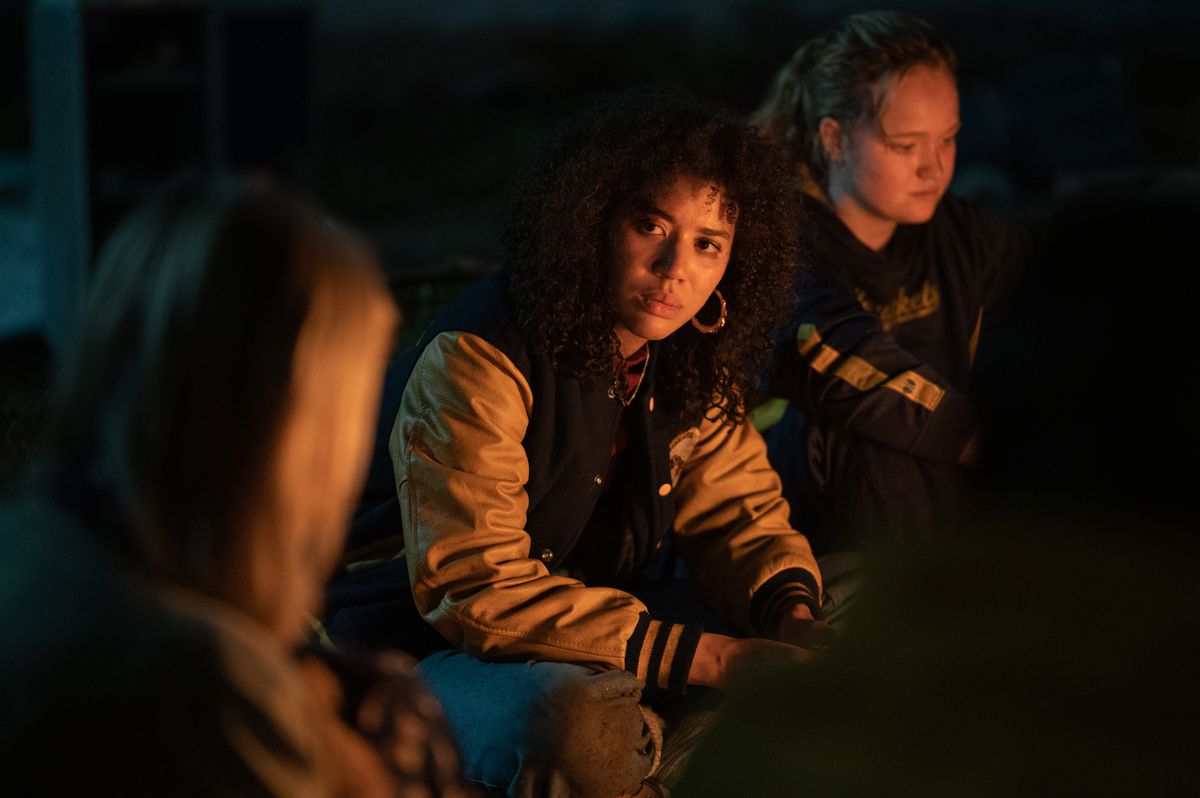 De tienerversie van Taissa, gespeeld door Jasmin Savoy Brown, zit naast de open haard in de wildernis, naast haar vriendin Van (gespeeld door Liv Hewson)
