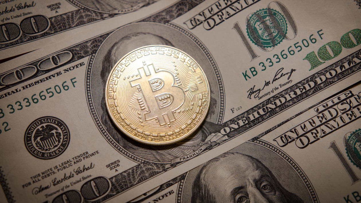100 ドル紙幣のベンジャミン フランクリンの顔を覆うビットコインの物理モデルの写真。