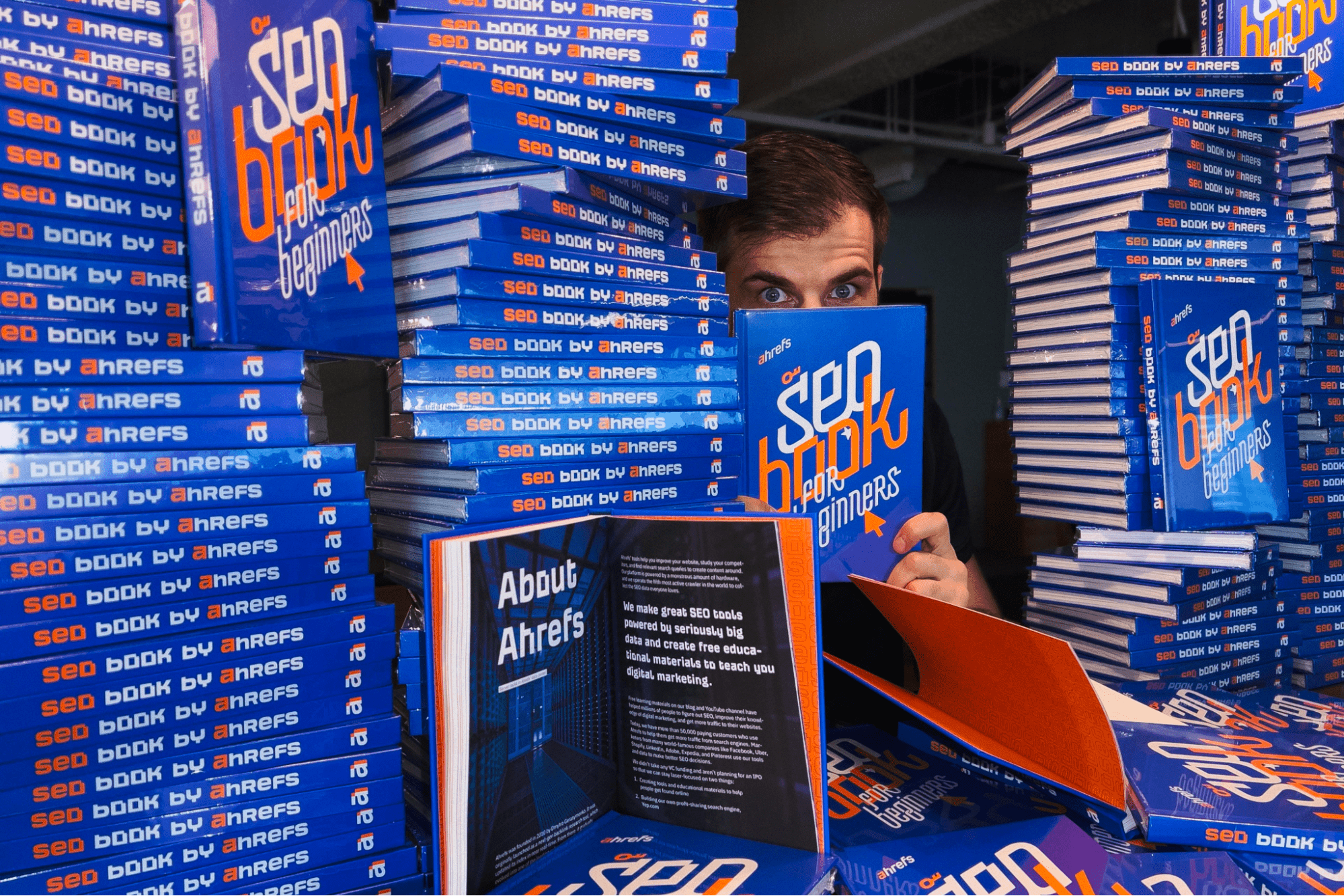 Ahrefs の CMO であるティム・ソウロ氏は、同社の書籍「SEO Book for Beginners」の山に囲まれている