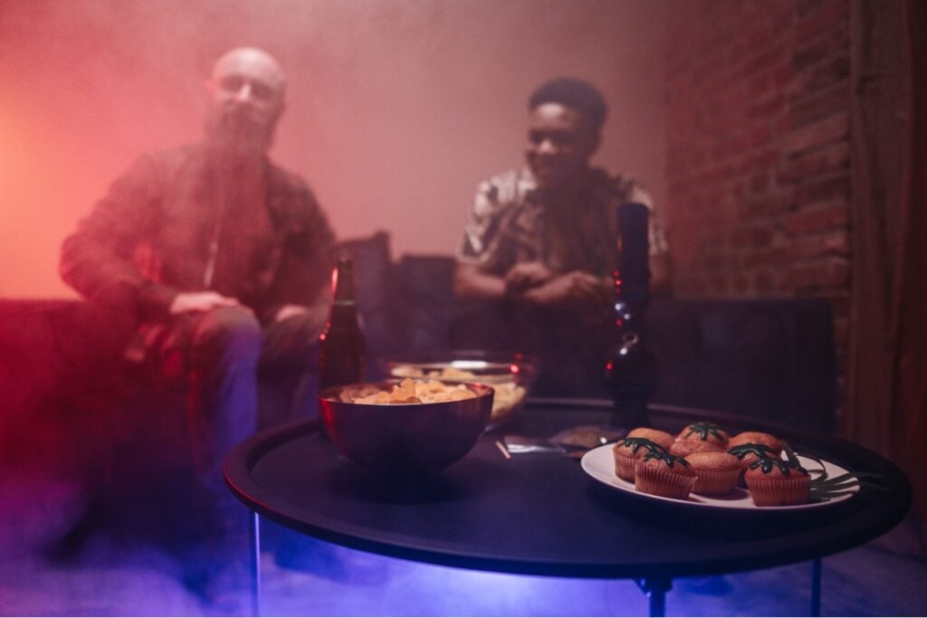 twee personen kijken naar marihuana-munchies op een tafel in een kamer vol rook