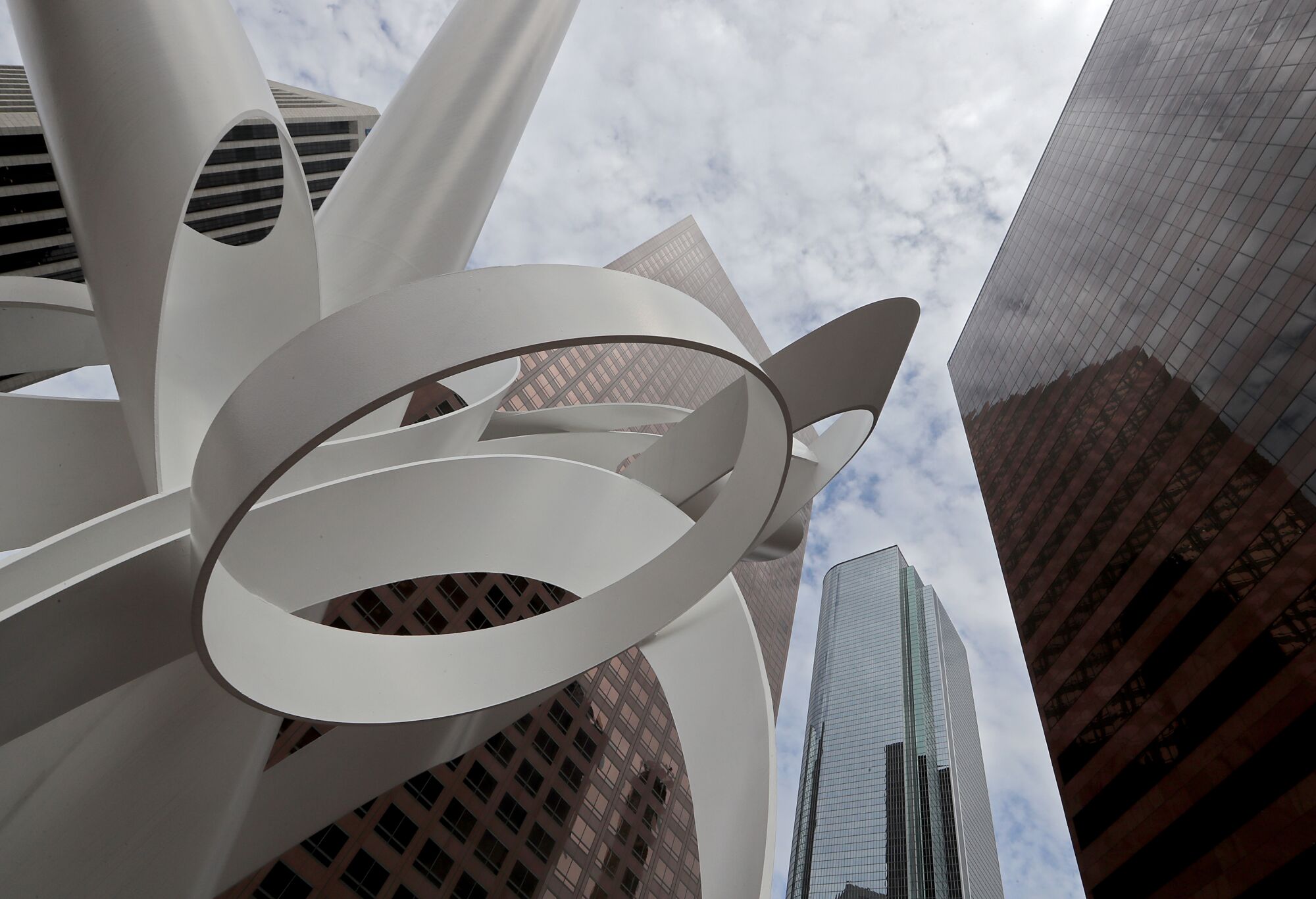 A low-angle frame of a white ribbon-like sculpture against skyscrapers and sky.