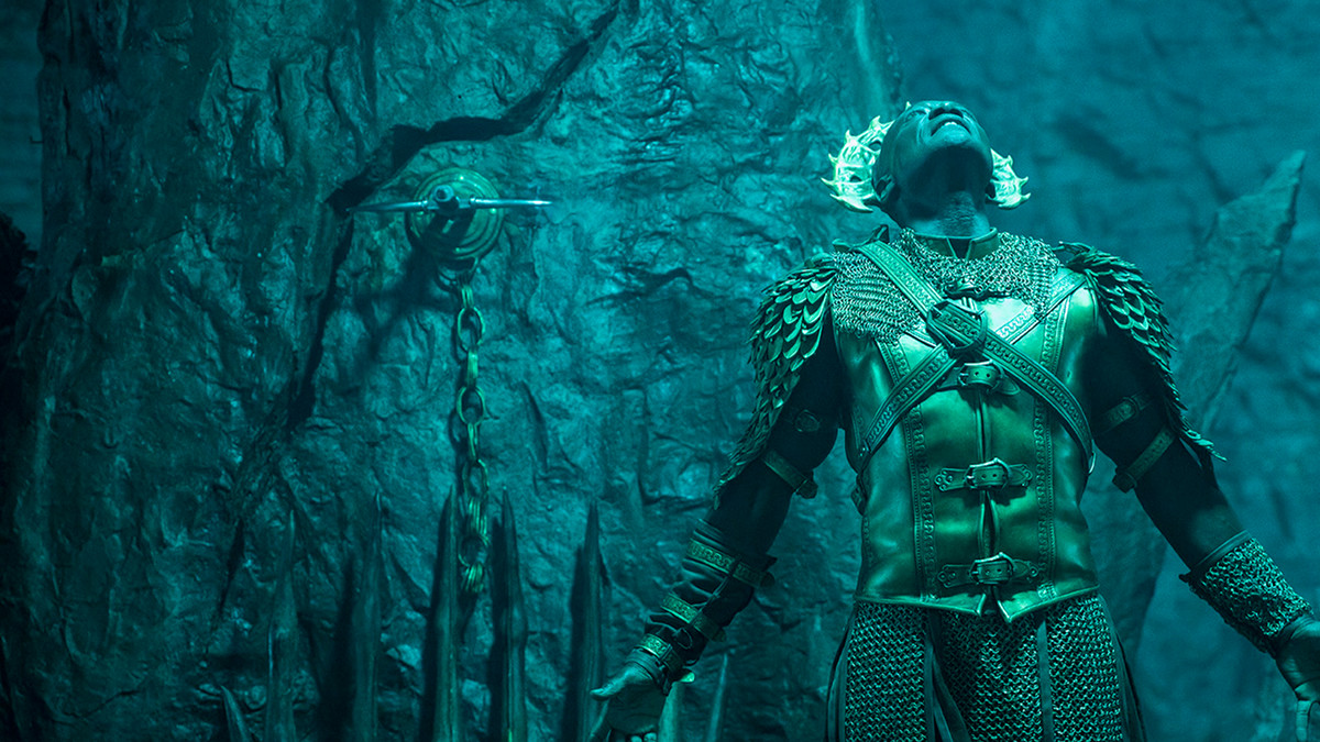 Peter Mensah als de aartsengel Michaël, starend naar een onbekende lichtbron met een stenen muur op de achtergrond in The Devil Conspiracy.