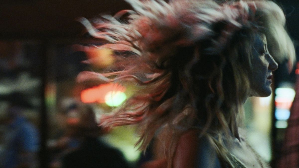 Andrea Riseborough, Leslie Rowland rolünde, To Leslie'de saçları rüzgarda çılgınca uçuşurken işlek bir caddede yürüyor.