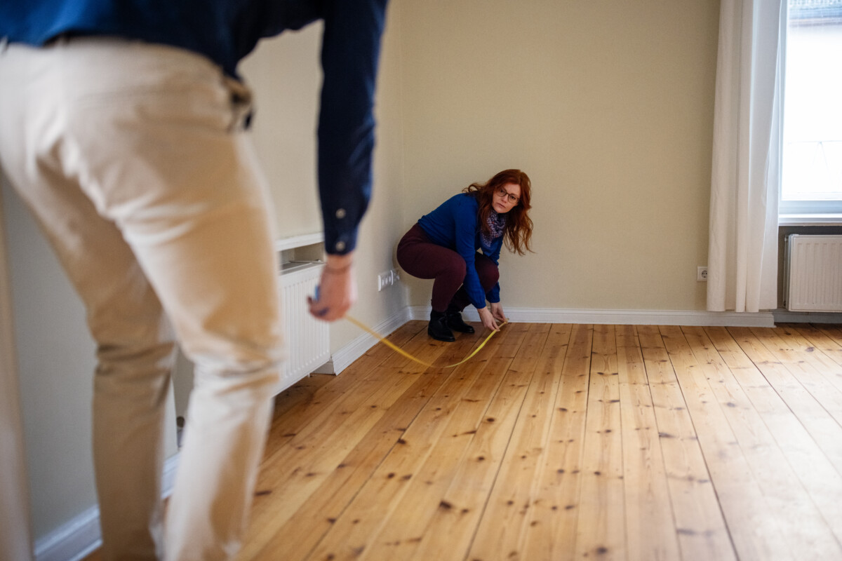 Mujer agachada mientras mide el piso de una casa nueva con un hombre