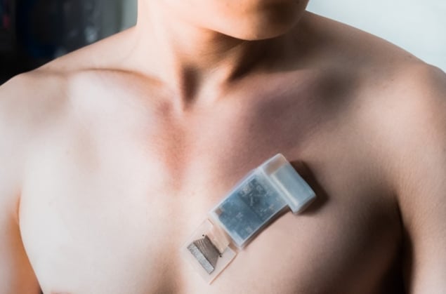 Una foto que muestra la parte superior del pecho desnudo de una persona, con el chip de ultrasonido adherido a la piel sobre el corazón. El chip es más pequeño que una tarjeta de crédito y no está conectado a ningún cable.