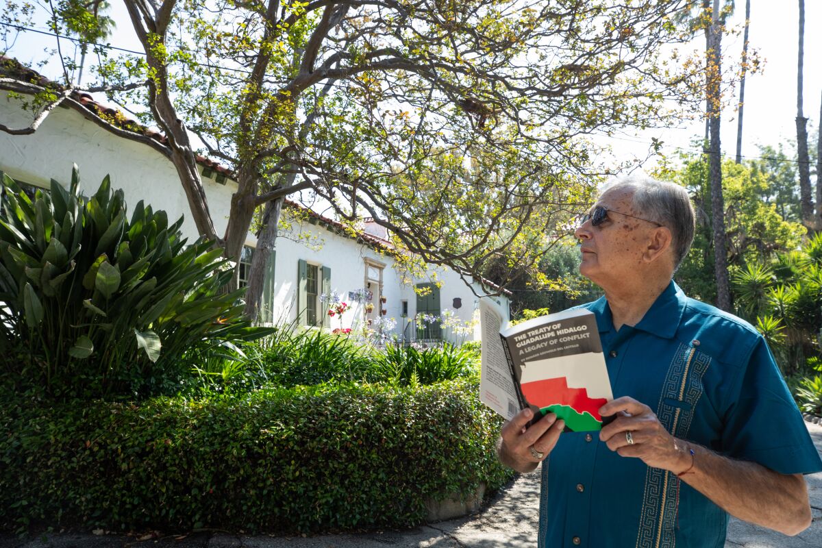 De gepensioneerde USC-professor Felix Gutierrez staat voor een klein huis omgeven door volwassen bomen en groen