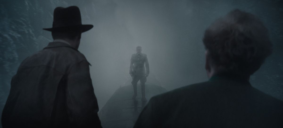 Indiana Jones (links) en Basil Shaw (rechts), met de rug naar de kijker gericht, confronteren slechterik Jurgen Voller, afgetekend in de mist, boven op een rijdende trein.