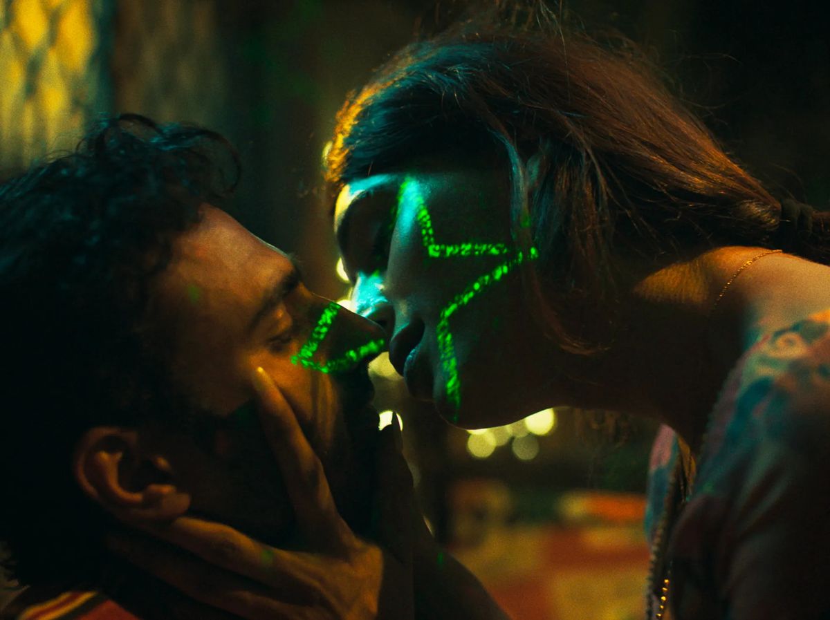 (LR) Ali Junejo와 Rasti Farooq가 Joyland에서 후자의 얼굴에 보이는 별 모양의 녹색 불빛으로 키스하기 위해 서로를 향해 몸을 기울이고 있습니다.
