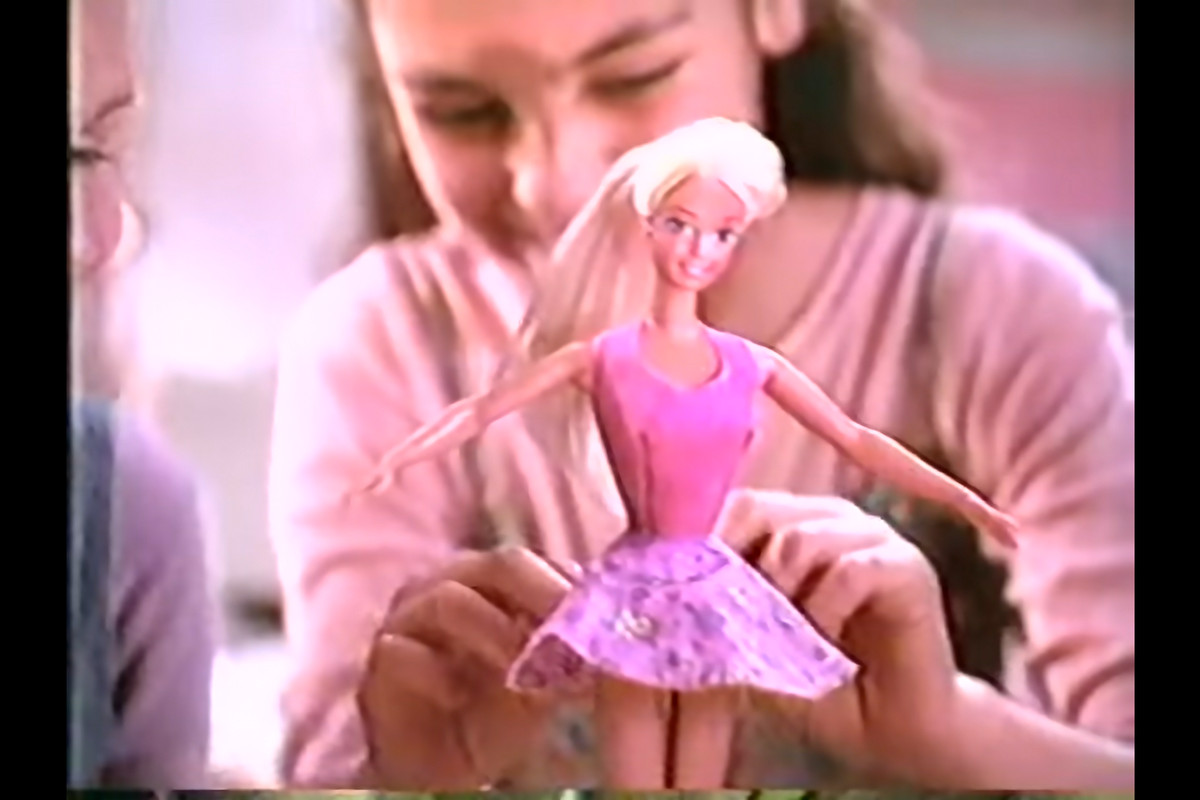 Uma jovem Mila Kunis colocando uma roupa na Barbie.