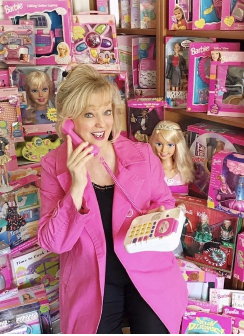 A voz da Barbie, Chris Lansdowne, cercada por produtos da Barbie.