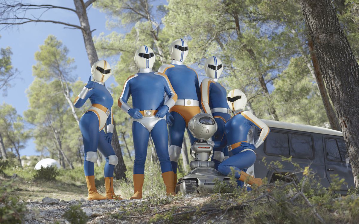 De vijf superhelden van Tobacco Force en hun robotmaatje poseren op een beboste heuvel in een still uit Smoking Causes Coughing