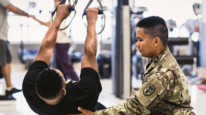 Physiotherapeut im Einsatztarnmuster hilft einem männlichen Patienten. Foto vom Army Enterprise Marketing Office (AEMO)