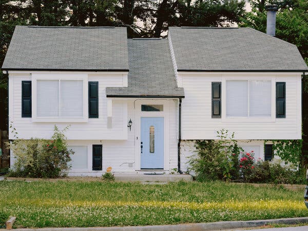 Một ngôi nhà màu trắng với cửa màu xanh lam, cửa chớp màu đen và mái nhà màu xám.
