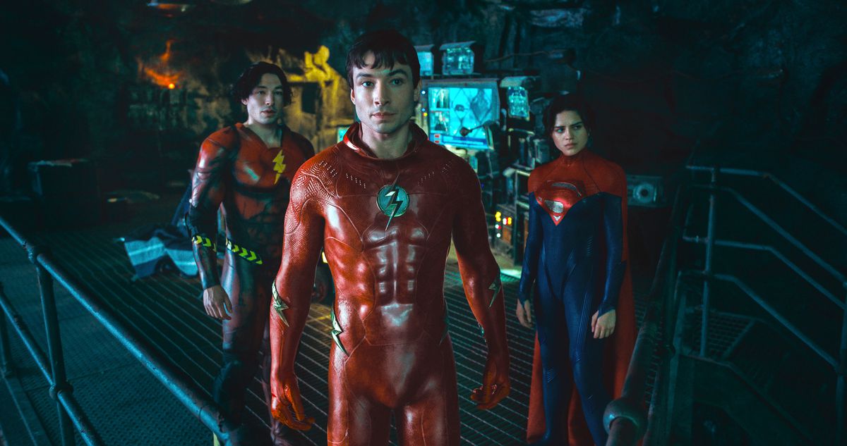 (L-R) Ezra Miller as Young Barry, Ezra Miller as Barry/The Flash and Sasha Calle as Supergirl standing in the Batcave in their costumes in The Flash.