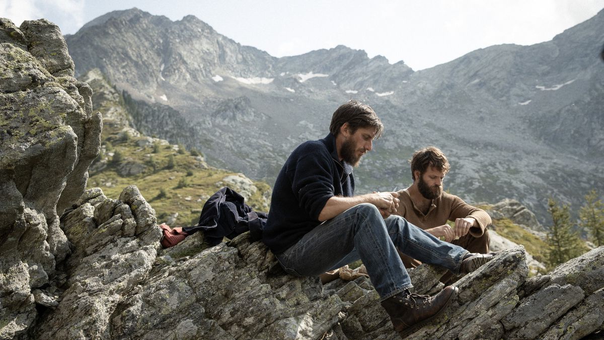 (LR) 루카 마리넬리(Luca Marinelli)와 알레산드로 보르기(Alessandro Borghi)가 에잇 산맥(The Eight Mountains)의 또 다른 더 큰 산맥이 내려다보이는 산에 앉아 있습니다.