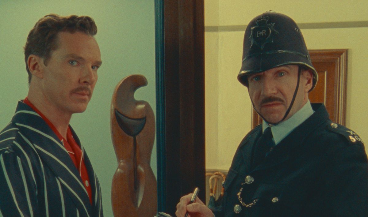 Benedict Cumberbatch (als Henry Sugar) en Ralph Finnes (verkleed als politieagent) kijken rechtstreeks in de camera in een scène uit Wes Andersons Netflix-film The Wonderful Story of Henry Sugar
