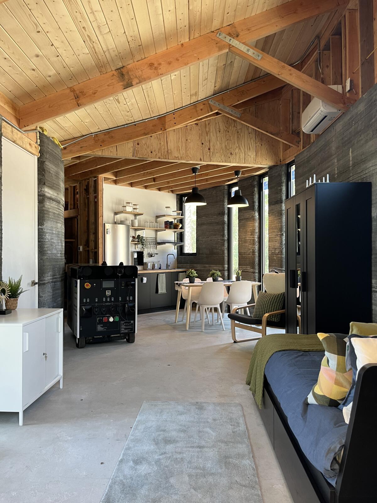 Una vista del espacio de un apartamento tipo estudio presenta un área para dormir en primer plano y una cocina suavemente curvada en la parte trasera.
