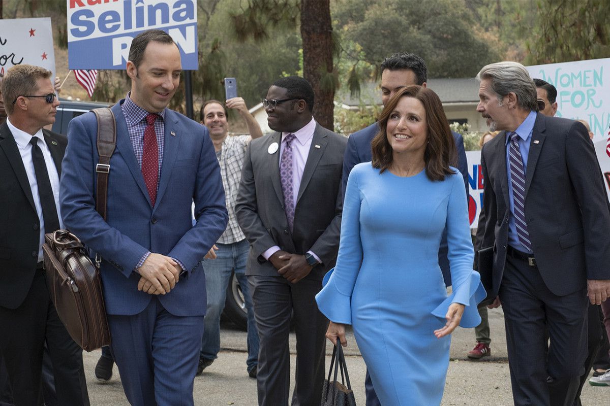 Julia Louis-Dreyfus, vestida con un vestido azul, camina con carteles de campaña a su alrededor, junto con Tony Hale, Sam Richardson y otro personal de apoyo.
