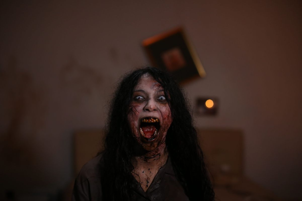 Một người phụ nữ với mái tóc đen dài, hàm răng sâu và làn da trắng với những đường gân đỏ thẫm đang la hét trong căn phòng nhếch nhác ở Blood Flower.