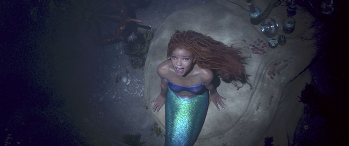 Halle Bailey với chiếc vây xanh và mái tóc đỏ của Ariel đang hát khi nhìn lên từ đáy đại dương trong Nàng tiên cá