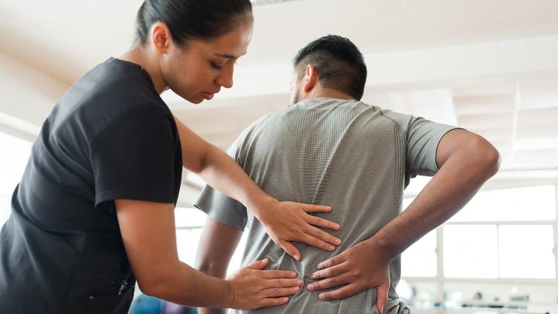 A massage therapist massaging a patient's back with both hands, photo by aldomurillo/Getty Images