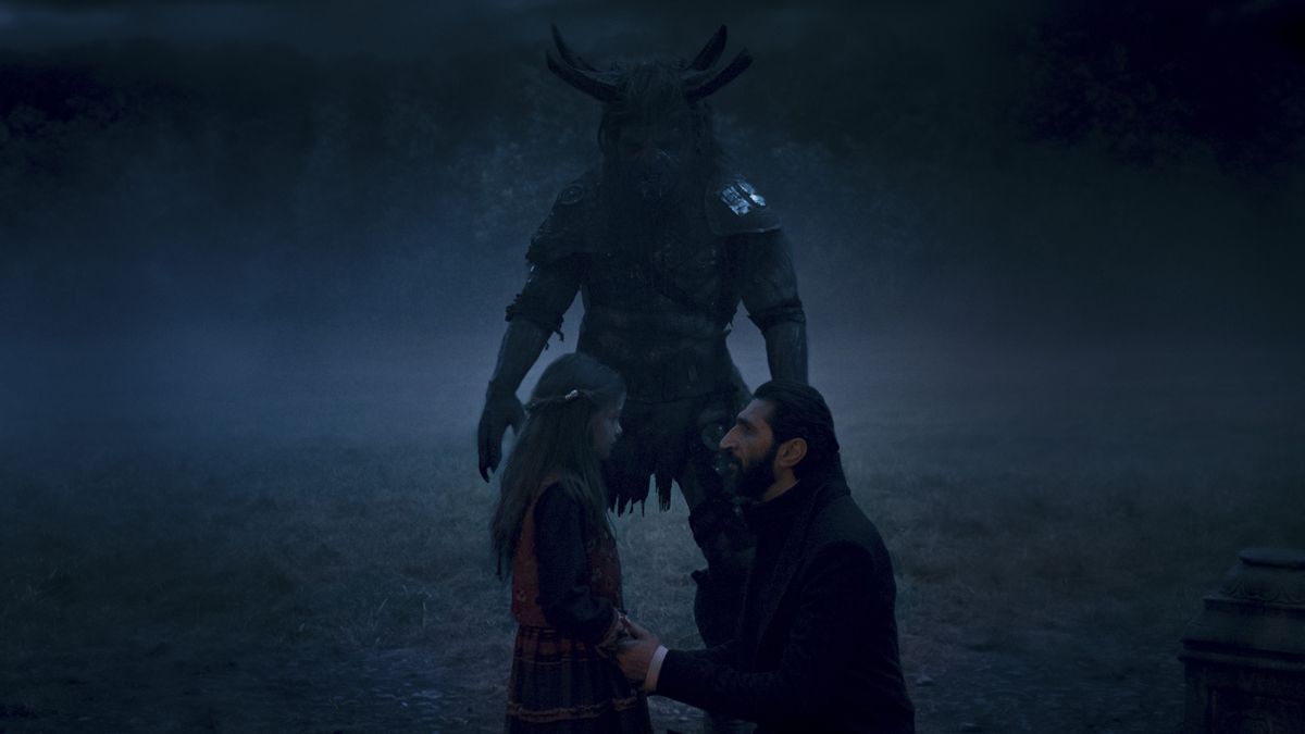 Ishamael (Fares Fares) se arrodilla y habla con una niña mientras Trolloc está a su lado.