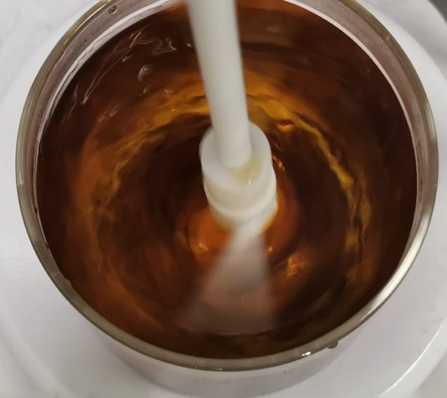 Photo showing a white plastic stirrer agitating amber-brown liquid in a metal container