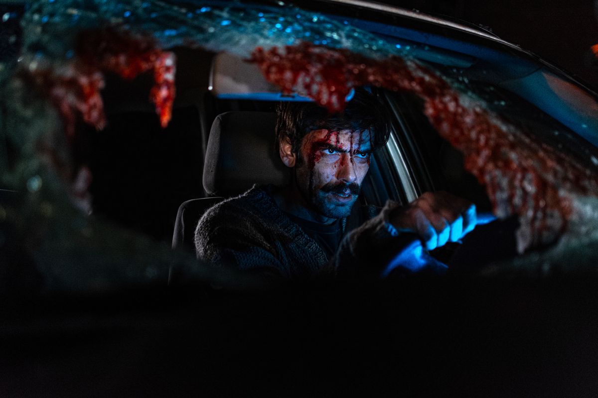 Ezequiel Rodríguez zit met zijn gezicht onder het bloed op de bestuurdersstoel van een auto met zijn handen aan het stuur in When Evil Lurks. De voorruit van de auto is verbrijzeld, met veel bloed.