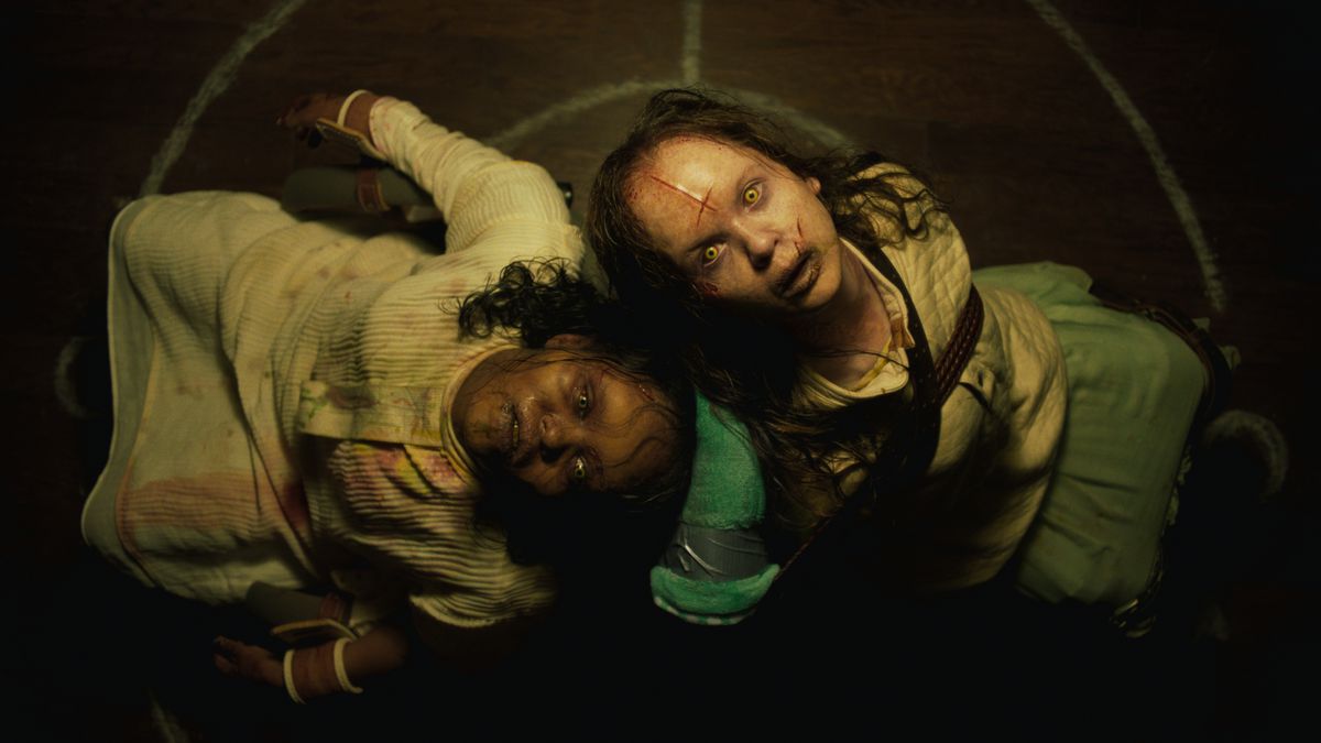 Twee bezeten, met littekens bedekte en gekneusde kinderen zitten rug aan rug op de grond en staren naar de camera boven hen in The Exorcist: Believer