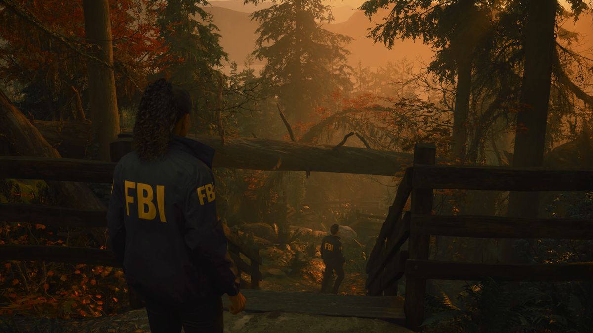 La agente del FBI Saga Anderson sigue a su compañero Alex Casey por un empinado sendero forestal en Alan Wake 2, con una hermosa puesta de sol de fondo.