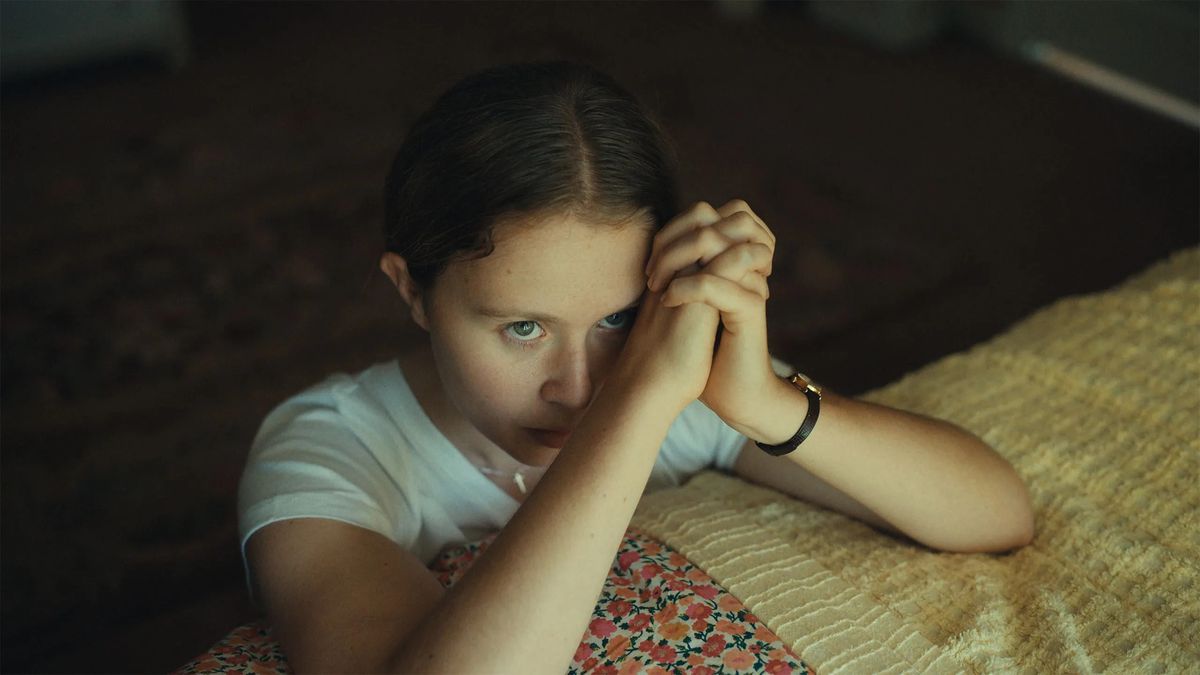 『スターリング・ガール』でベッドの前にひざまずいて祈っているジェム・スターリング役のエリザ・スカンレン。