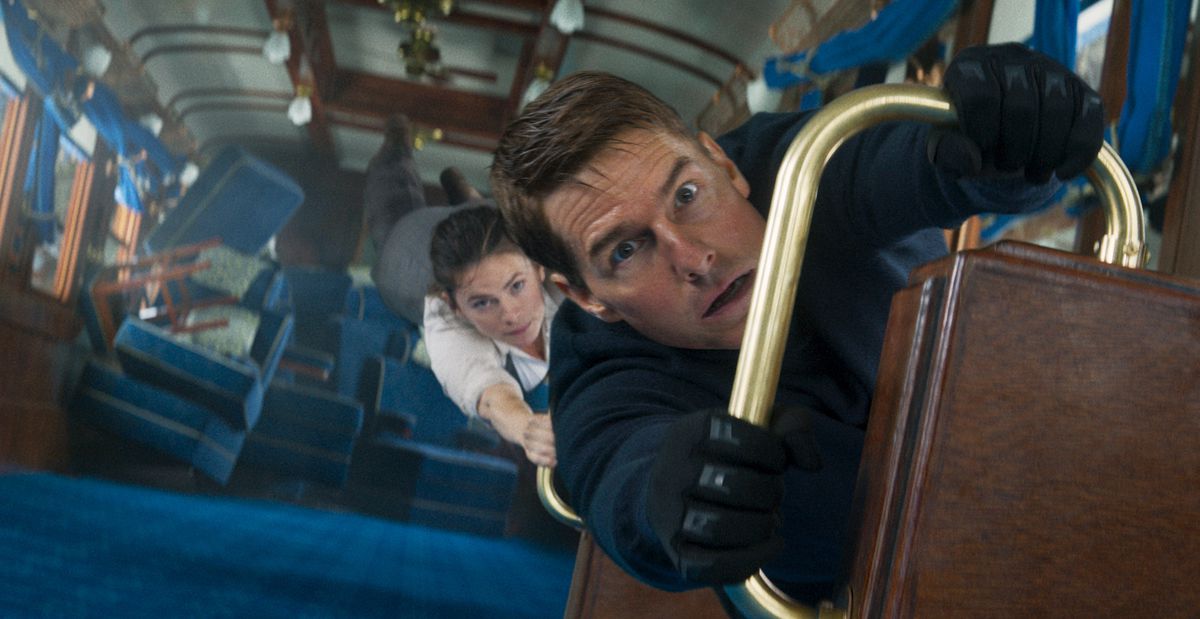 Tom Cruise terwijl Ethan Hunt zich vasthoudt aan een reling in een verticaal gedraaide treinwagon terwijl Hayley Atwell zich aan hem vastklampt in Mission: Impossible – Dead Reckoning Part One