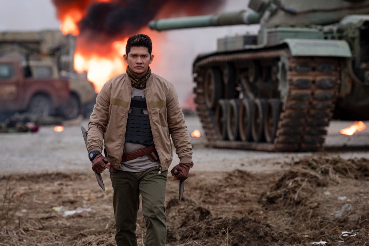 Iko Uwais walks away from an explosion in Expend4bles, holding spiked tonfa weapons.