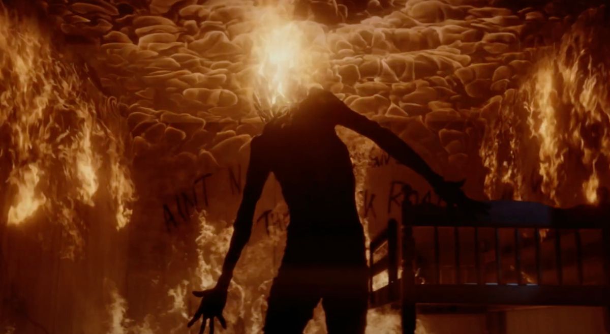 Een figuur zonder hoofd staat in een kamer die in vlammen opgaat, terwijl een vuurpluim uit hun nek spuwt in Dark Harvest.
