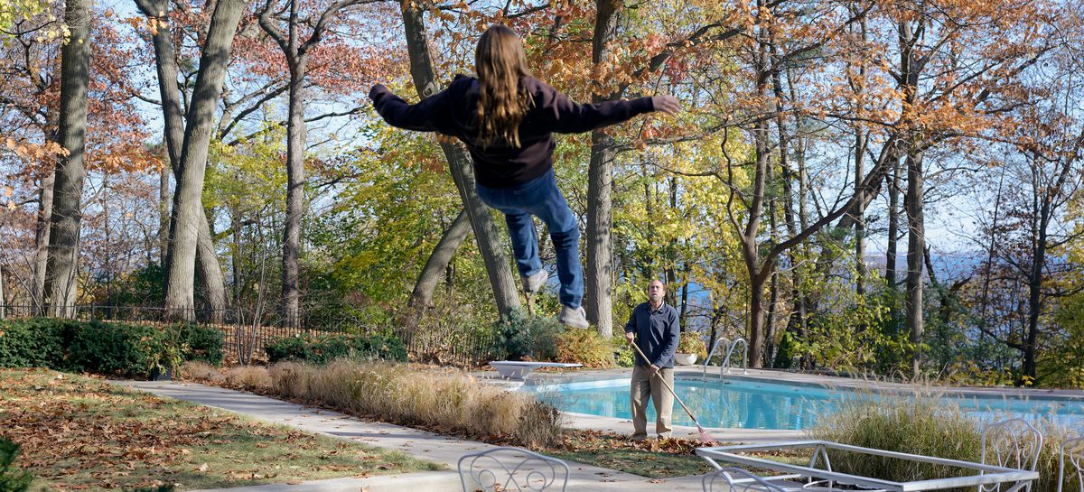 Schlubby-professor Paul Matthews (Nicolas Cage) staat bij een zwembad in de achtertuin herfstbladeren te harken en kijkt op terwijl een tienermeisje in een trui voor hem de lucht in begint te zweven in de A24-film Dream Scenario
