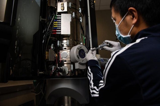 Portant un masque et des gants, Yaobin Xu insère un échantillon dans un microscope électronique à transmission pour examiner le fonctionnement d'une batterie rechargeable
