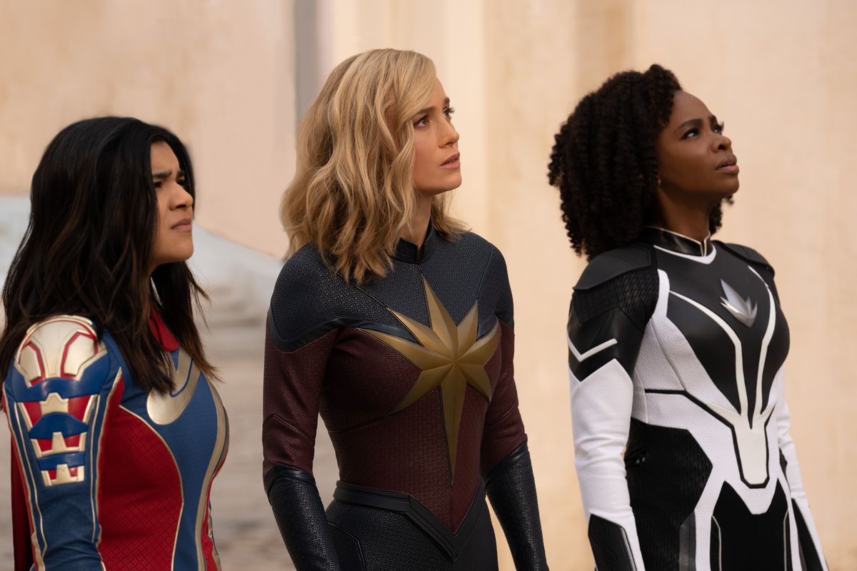 Iman Vellani como Ms. Marvel/Kamala Khan, Brie Larson como Captain Marvel/Carol Danvers y Teyonah Parris como Captain Monica Rambeau están juntas disfrazadas, todas mirando hacia arriba, en la película de Marvel Cinematic Universe The Marvels.