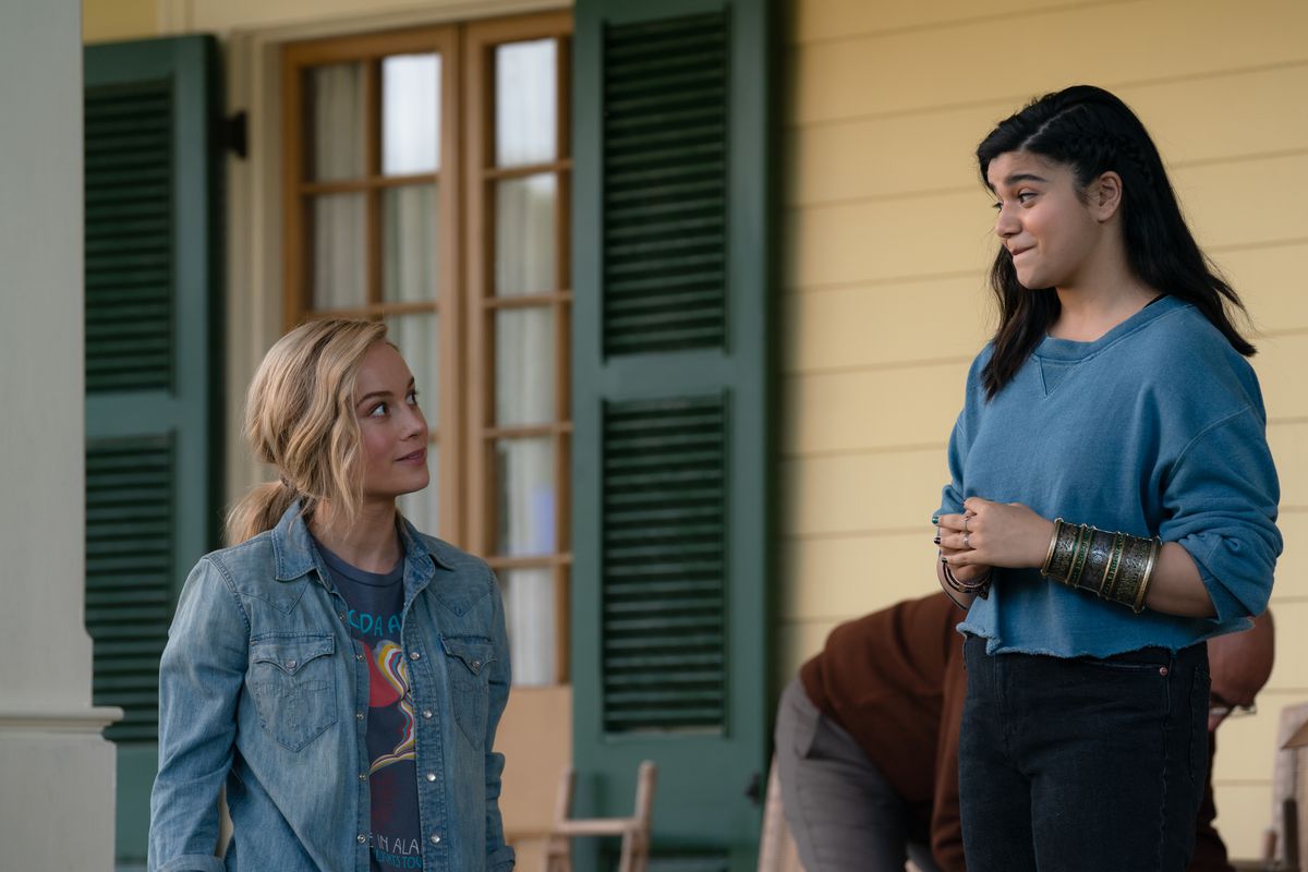 Marvel Sinematik Evreni filmi The Marvels'da Kaptan Marvel/Carol Danvers rolünde Brie Larson ve Bayan Marvel/Kamala Khan rolünde Iman Vellani açık havada verandada duruyor ve birbirlerine gülümsüyorlar
